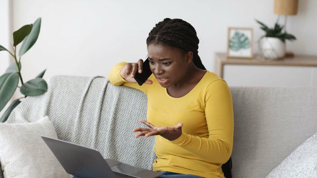 Young black woman on sofa with laptop and cellphone looking frustrated